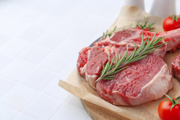 Piece of raw beef, rosemary and tomatoes on white tiled table, closeup. Space for text