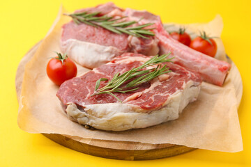 Pieces of raw beef, rosemary and tomatoes on yellow table, closeup