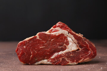 One piece of raw beef on brown textured table against black background, closeup