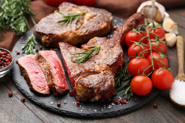 Pieces of delicious beef meat, spices and tomatoes on wooden table, closeup