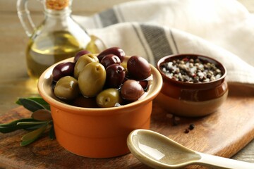 Tasty olives in bowl, leaves, oil and spices on wooden table, closeup