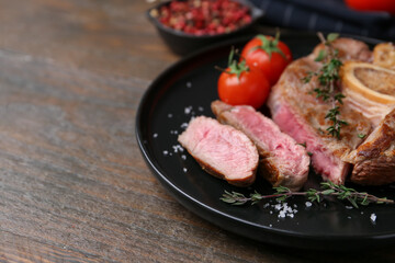 Pieces of delicious beef meat, spices and tomatoes on wooden table, closeup. Space for text
