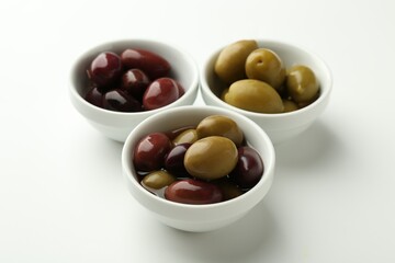 Tasty marinated olives in bowls on white table, closeup
