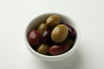 Tasty marinated olives in bowl on white table, closeup