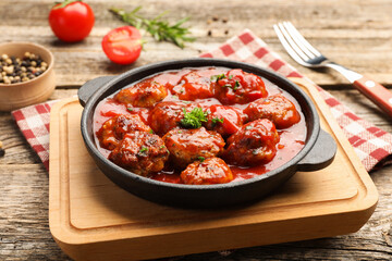 Delicious meatballs with tomato sauce in baking dish and spices on wooden table, closeup