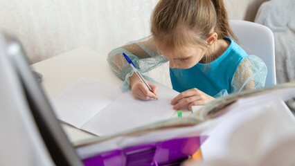 Little school girl sit at table at home write in exercise book prepare homework alone.