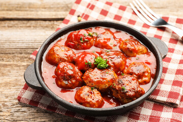 Delicious meatballs with tomato sauce in baking dish on wooden table, closeup
