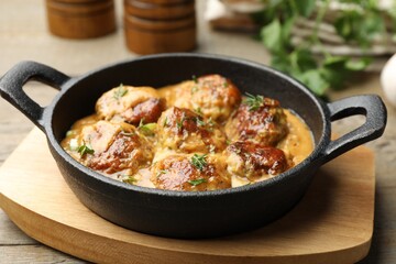 Delicious meatballs with gravy cream sauce and herbs on wooden table, closeup