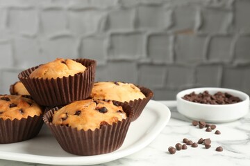 Delicious muffin with chocolate chips on white marble table, closeup
