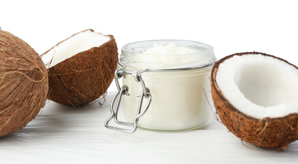 Organic coconut cooking oil in jar and fresh fruits on wooden table against white background