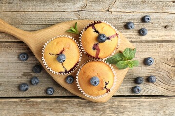 Delicious muffins with blueberries and mint on wooden table, flat lay