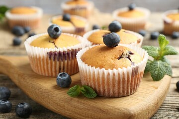 Delicious muffins with blueberries and mint on wooden table, closeup