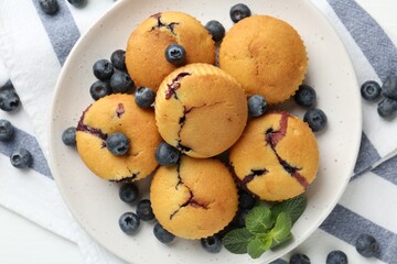 Delicious muffins with blueberries and mint on white table, top view