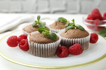 Delicious muffins with raspberries and mint on white table, closeup
