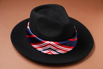 Black hat with striped scarf on brown background, closeup