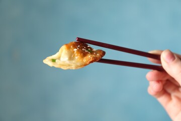 Woman holding tasty fried gyoza (dumpling) with chopsticks on light blue background, closeup