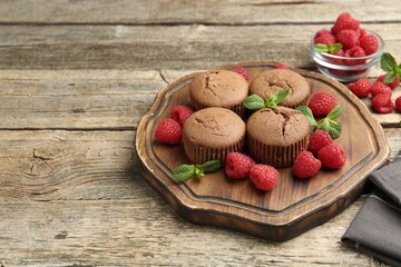 Delicious muffins with raspberries and mint on wooden table. Space for text