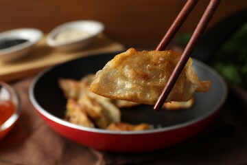 Holding tasty fried gyoza (dumpling) with chopsticks on table, closeup