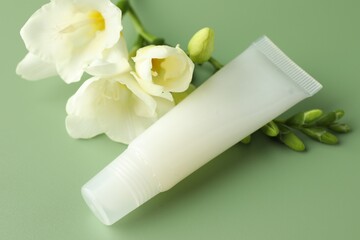 Lip balm and freesia flowers on light green background, closeup
