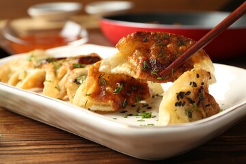 Taking tasty fried gyoza (dumpling) with chopsticks on wooden table, closeup