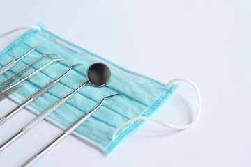 Collection of dental instruments on white background. Dental mirror, tweezers and several hooks on disposable medical mask. Diagnostic dental instrument set. Oral and dental health concept. Medicine