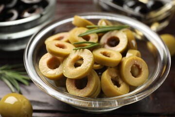 Delicious marinated olive rings, whole one and rosemary on wooden table, closeup