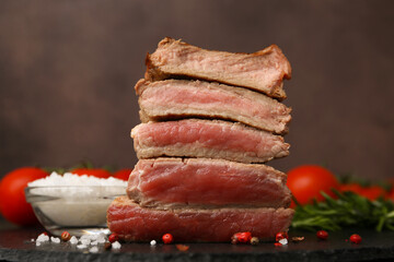 Delicious sliced beef tenderloin with different degrees of doneness and spices on table against brown background, closeup