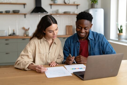 Young multiracial couple reviewing finances on laptop in modern kitchen - Powered by Adobe