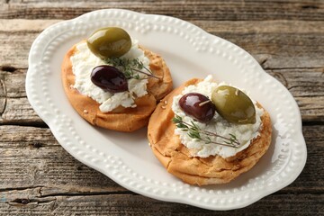 Delicious sandwiches with marinated olives, cream cheese and thyme on wooden table, above view