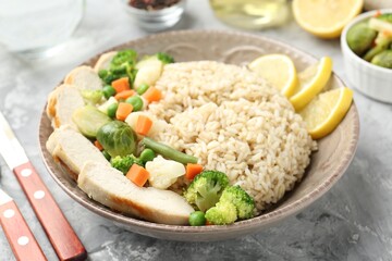 Delicious brown rice with chicken, vegetables and lemon slices served on grey textured table, closeup