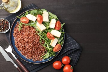 Delicious brown rice with chicken, arugula and tomatoes served on black wooden table, flat lay. Space for text