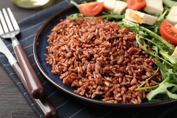 Delicious brown rice with chicken, arugula and tomatoes on black wooden table, closeup