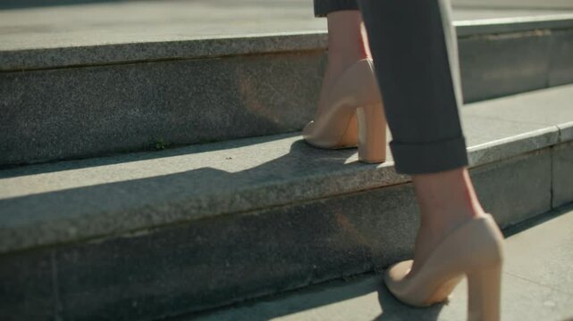 Lower leg view of woman walking in high heels on interlocked pavement ascending concrete steps, sunlight casting sharp shadow, focus on movement, footwear, business attire, and urban setting