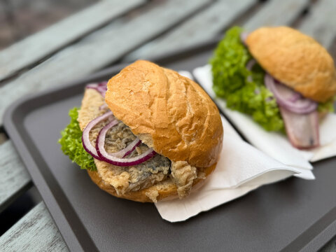 Traditional north germany snack street food fish sanwich Fischbroetchen fried herring with onion and salad leaves in a wheat bun on a table close up on Fischmarkt in Hamburg