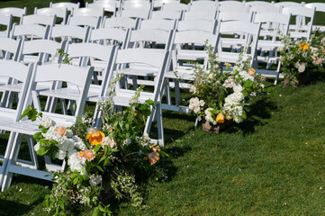 White ceremony chairs with floral aisle arrangements on green lawn