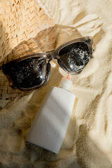 A straw hat, glasses and a tube of sunscreen are lying on the sand on the beach. The concept of recreation. protection from the sun. There is a place for text or advertising.