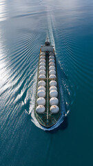 Aerial view of a cargo ship carrying large white tanks sailing on a blue ocean with rippling waves.