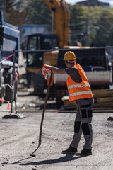 Naklejka premium Construction worker using a tool for site preparation during the day near heavy machinery and equipment