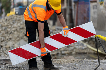 Construction worker placing safety barrier at roadwork site during daylight hours in urban setting