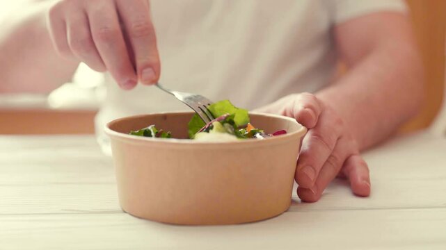 Closeup of man eating a fresh healthy salad from a zero waste container to go. Food delivery, healthy food concept.