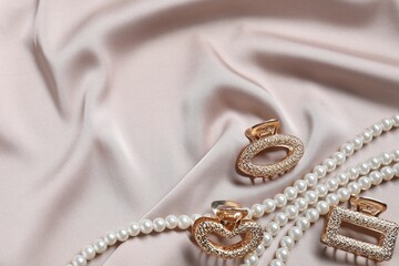 Beautiful hair clips and pearl necklace on beige fabric, flat lay. Space for text