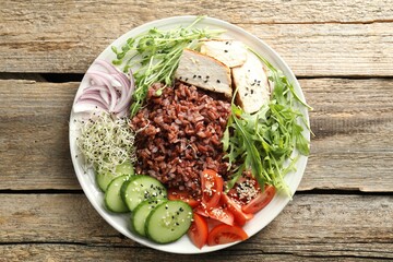 Delicious salad with brown rice on wooden table, top view