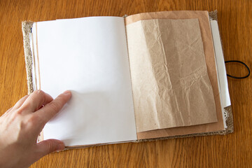 Female hand pointing at page in blank notebook homemade from kraft paper and burlap on wooden...
