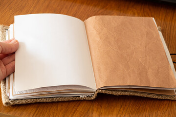 Female hand pointing at page in blank notebook homemade from kraft paper and burlap on wooden...