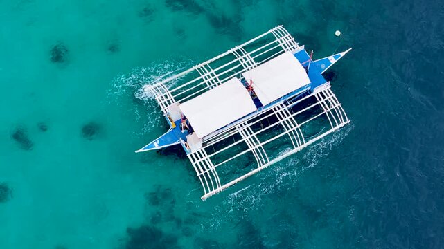 Close up of traditional Philippine island hopping boat sailing in turquoise color water over coral reef. Aerial 4K top view drone video footage