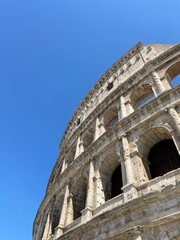 Fototapeta premium The majestic Colosseum in Rome, Italy, stands as a timeless icon of ancient Roman engineering and culture. This monumental amphitheater is bathed in sunlight against a vibrant blue sky.