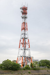 A tall transmission tower is painted in orange and white. These towers are important infrastructure for radio, tv, and cellular communications which helped modernize cities in Asia.
