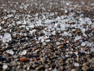 Close-up of white salt grains on icy sidewalk surface in the winter. Applying salt to keep roads clear and people safe in winter