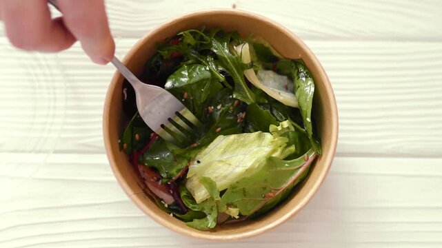 Closeup of man eating a fresh healthy salad from a zero waste container to go. Food delivery, healthy food concept.