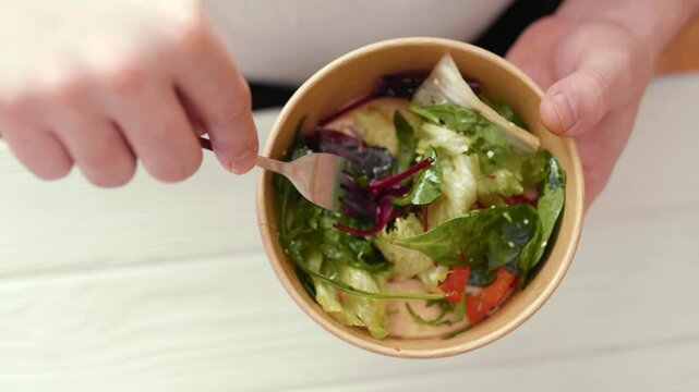 Closeup of man eating a fresh healthy salad from a zero waste container to go. Food delivery, healthy food concept.